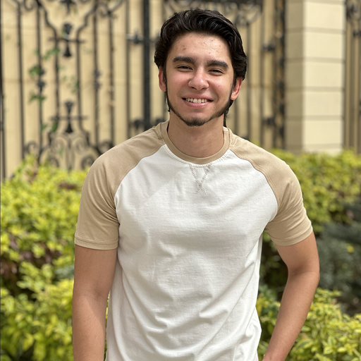 Mostafa Abdelsalam smiling in a cream raglan tee in front of an iron gate